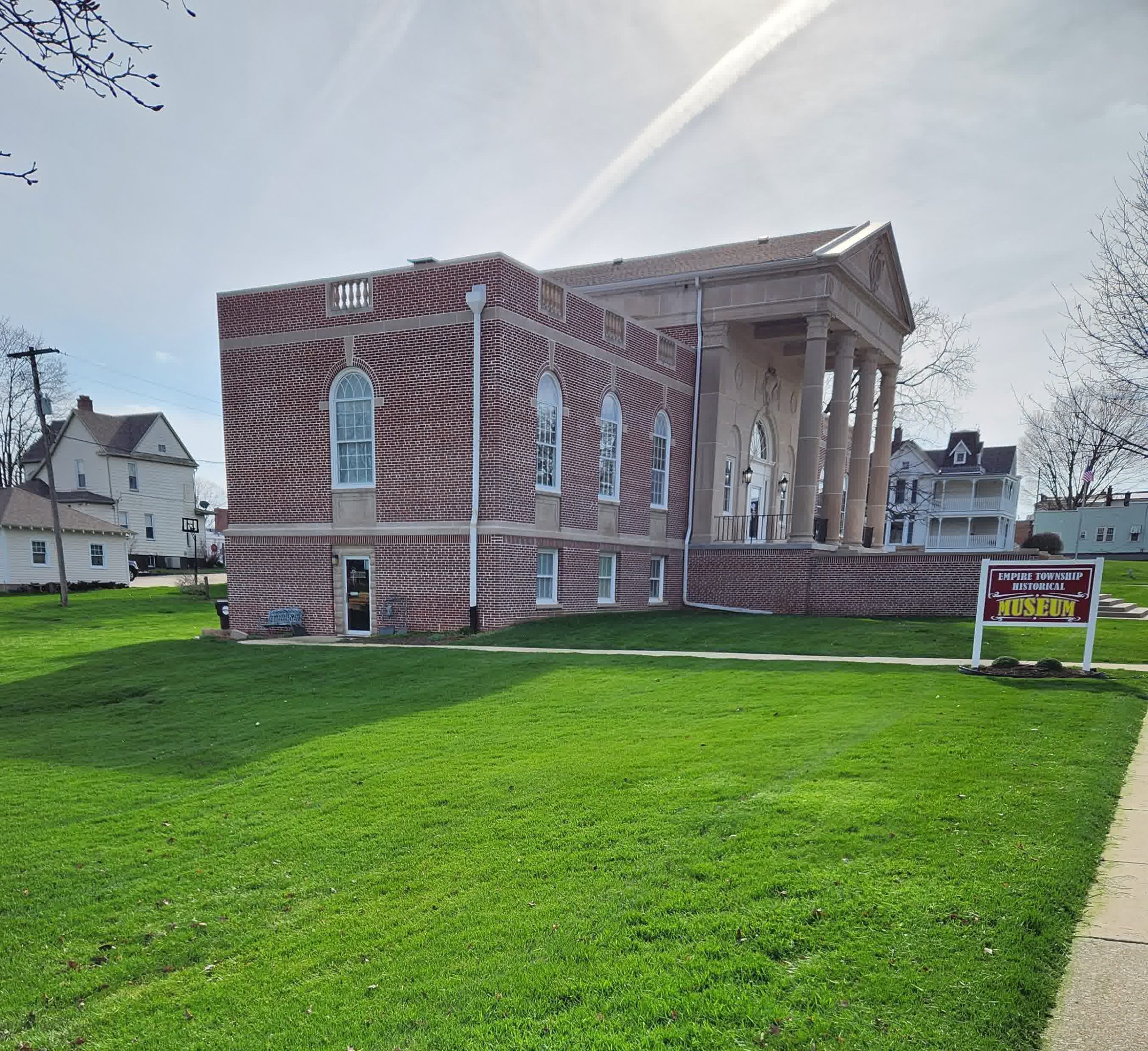 Historic brick building with tall columns and arched windows sits on a manicured green lawn, identified as Empire Township Historical Museum.
